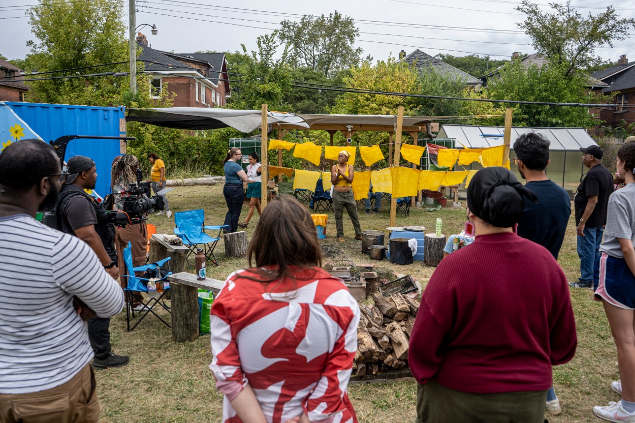 A group stands outdoors, watching an art display with yellow fabric pieces hanging on a line.