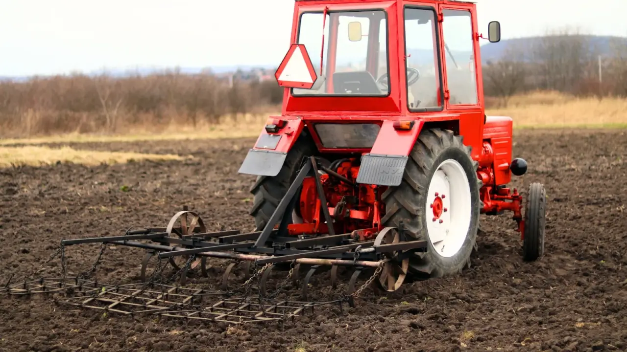 A red tractor pulling a chisel plow across a large field to improve soil drainage.